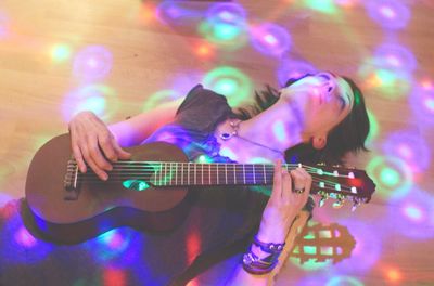 Young woman playing guitar while lying on hardwood floor