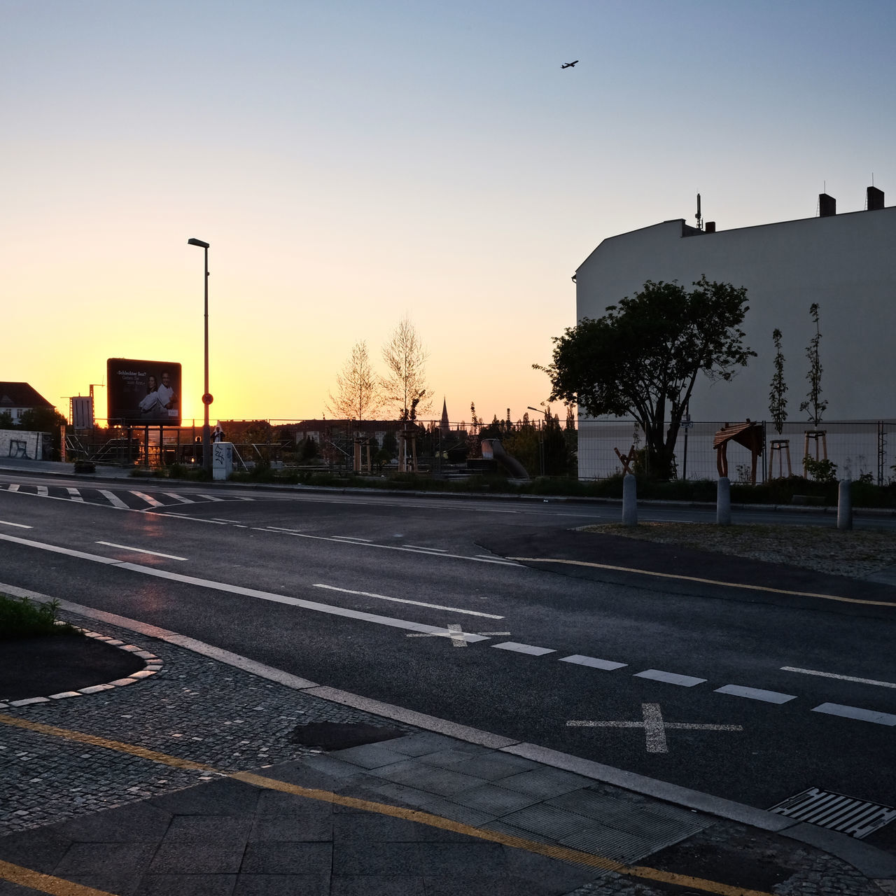 transportation, sunset, road marking, road, clear sky, street light, street, building exterior, sky, built structure, architecture, car, silhouette, tree, the way forward, city, incidental people, mode of transport, land vehicle, outdoors