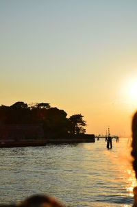 Silhouette trees by river against clear sky during sunset