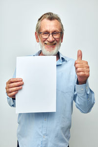 Portrait of smiling businessman holding paper against white background