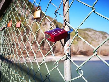 Close-up of padlocks on chainlink fence against sky