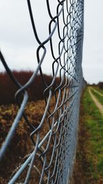 Close-up of chainlink fence on field against sky