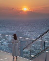 Rear view of woman looking at cityscape during sunset