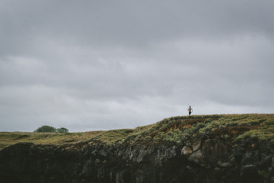 Distant view of woman jogging on mountain against cloudy sky