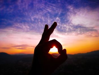 Cropped hand gesturing ok sign against sky during sunset