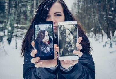 Young woman showing photographs on mobile phones in forest during winter