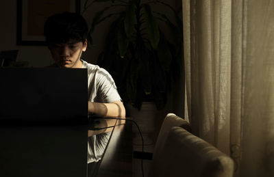 Portrait of teenage asian boy using laptop indoor with sunlight and shadow