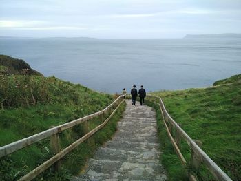 Rear view of men walking by sea against sky