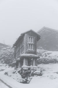 Snow covered houses by building against clear sky