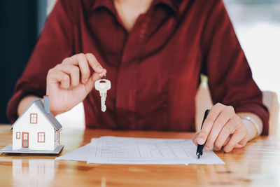 Midsection of estate agent holding key over table at office