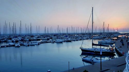 Sailboats moored in harbor at sunset