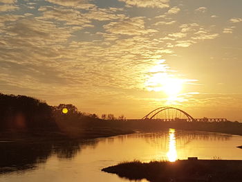 Silhouette bridge over river against sky during sunset