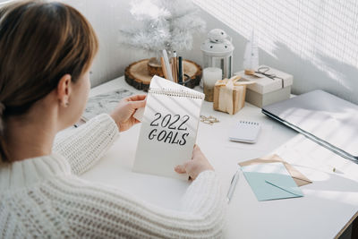 2022 goals, new year resolution. woman in white sweater writing text 2022 goals in open notepad on