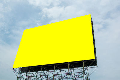 Low angle view of yellow sign against sky