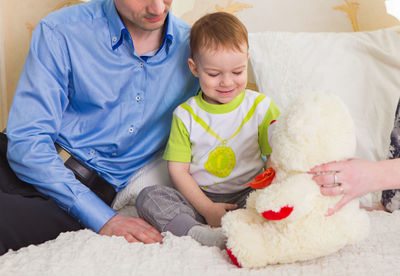Midsection of father with son sitting with toy sitting on bed