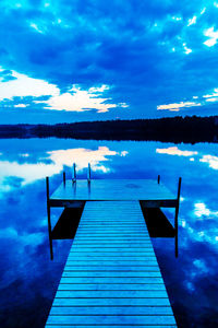 Pier on calm lake against cloudy sky