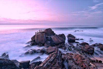 Rocks in sea against sky during sunset