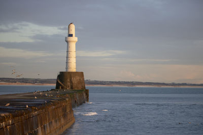 Lighthouse by sea against sky