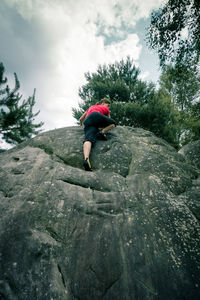 Low angle view of woman bouldering on rock against cloudy sky