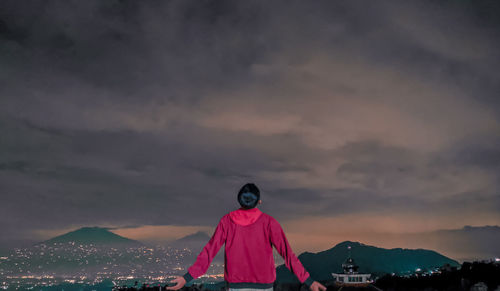 Rear view of woman standing on mountain against sky during sunset