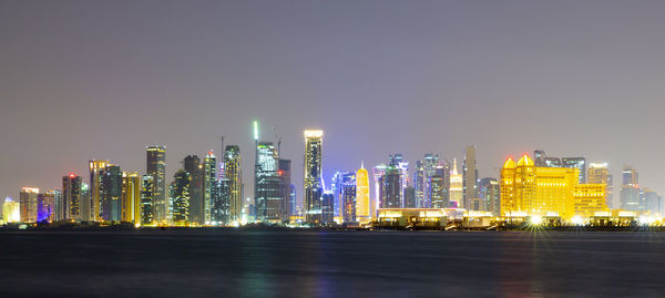 Illuminated modern buildings in city against sky at night