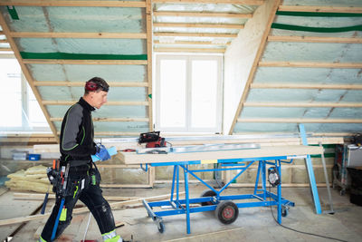 Side view of manual worker holding metallic plank while walking at construction site