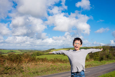 Portrait of boy standing with arms outstretched standing against sky