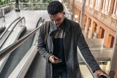 Smiling man using mobile phone standing on escalator