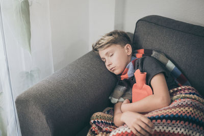 High angle view of boy sleeping with hot water bottle on sofa at home