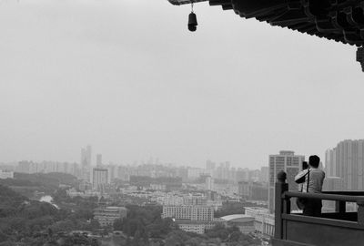 Rear view of man sitting on buildings against sky