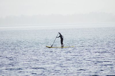 Man paddleboarding in sea during foggy weather