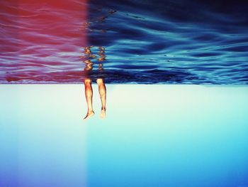 Upside down image of human legs in sea against blue sky