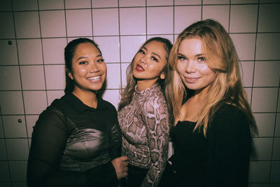 Portrait of smiling young multiracial female friends against white wall at nightclub