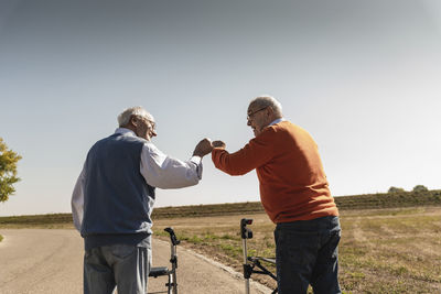 Two old friends with wheeled walkers, greeting in the street