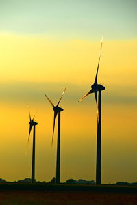 Silhouette wind turbines on field against sky during sunset