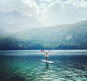 Rear view of woman paddleboarding on lake against mountain
