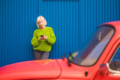 Woman using mobile phone while standing by red car