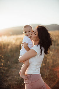 Side view of mother kissing son while standing on land during sunset