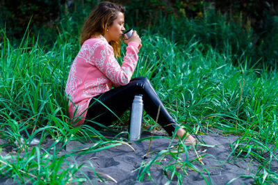 Full length of woman drinking water while sitting on grass