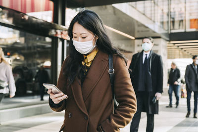 Woman with face mask walking in street using smartphone