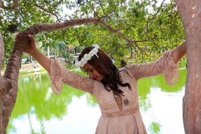Woman wearing flowers while standing by trees against lake