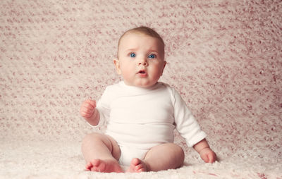 Portrait of cute baby girl sitting on bed