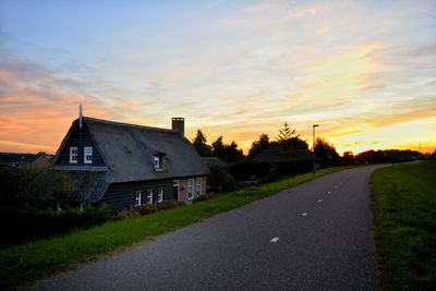 Road amidst buildings against sky during sunset