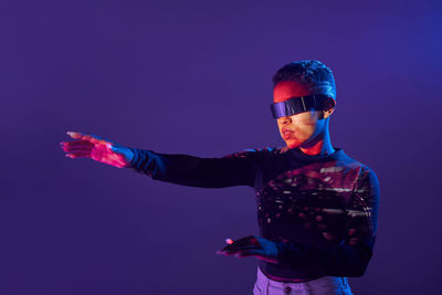 African american martial female with short hair in trendy vr goggles standing on purple background with outstretch arms in studio