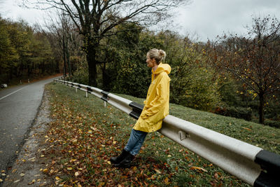 A serene middle-aged woman in a yellow raincoat walks in rainy weather in the countryside.