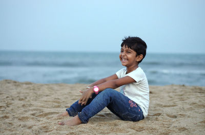 Happy young woman sitting on shore at beach against sky