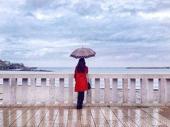 Rear view of woman standing by railing against cloudy sky