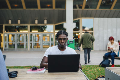 Young male student concentrating while e-learning on laptop in university