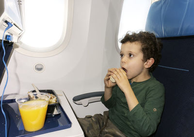 Cute little boy in airplane seat eating while looking at the screen