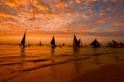 Sailboats sailing on sea against orange sky